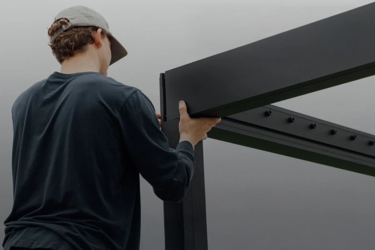 Darbininkas montuoja pergolos konstrukciją be silikono, naudodamas modernią tvirtinimo sistemą.